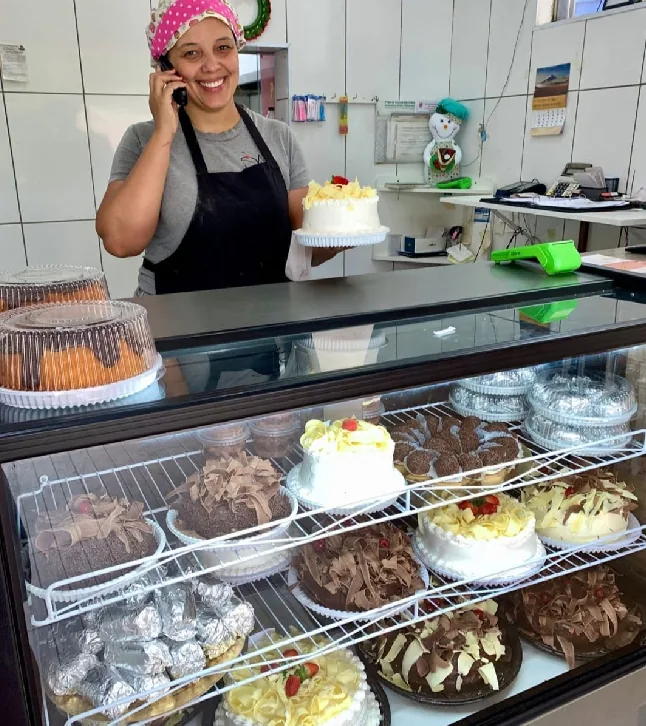 Atendente ao telefone atrás da vitrine de bolos da Dona Maria